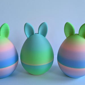 May include: Three pastel Easter eggs with bunny ears. The eggs are ombre with shades of pink, blue, and green.