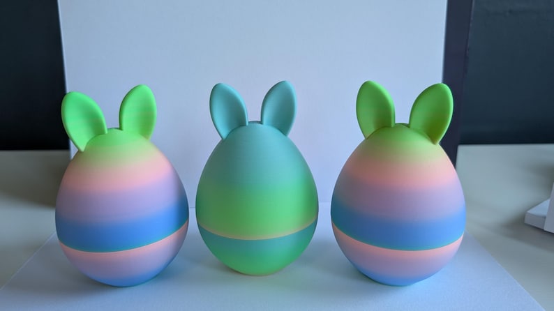 May include: Three pastel Easter eggs with bunny ears. The eggs are ombre with shades of pink, blue, and green.