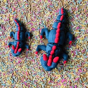 May include: Two blue and red play dough dragons on a background of colorful sprinkles.