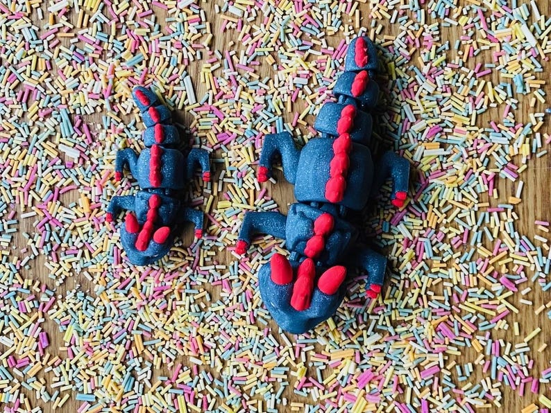 May include: Two blue and red play dough dragons on a background of colorful sprinkles.