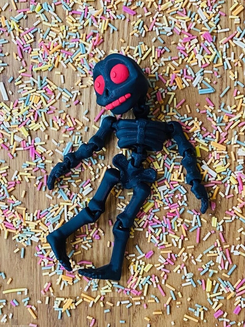 May include: A black articulated skeleton toy with a red skull lying on a surface covered in colorful sprinkles.