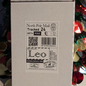 May include: A white cardboard box with "North Pole Mail" and "Tracked 24" printed on it. The box has a "Nice List Approved" stamp and a "Chimney Delivery Only" label. The name "Leo" is printed on the box.