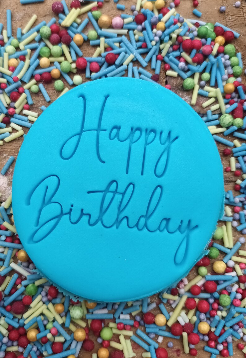 May include: A blue round cake topper with the words "Happy Birthday" in white script.