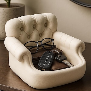 May include: A cream-coloured, miniature sofa-shaped organiser holds eyeglasses, a car key fob, a key, and two small brown leather wallets. The sofa has a tufted back and curved arms, sitting on a dark brown surface.