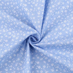 Könnte beinhalten: Ein Nahaufnahme eines hellblauen Stoffes mit einem weißen Blumenmuster. Der Stoff ist weich und glatt, und die Blumen sind klein und zart.