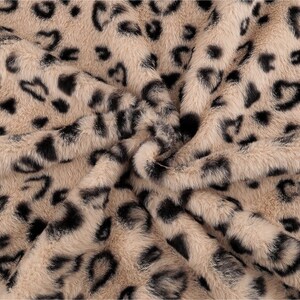 Könnte beinhalten: Nahaufnahme eines Kunstfellstoffs mit Leopardenmuster. Der Stoff hat einen beigefarbenen Grundton mit schwarzen Flecken und herzförmigen Markierungen. Das Material ist weich und plüschig, mit einer strukturierten Oberfläche.