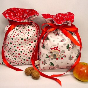 Könnte beinhalten: Zwei festliche Stoffgeschenktüten mit roten Schleifen. Eine Tasche hat ein Muster aus roten, grünen und grauen Sternen auf weißem Grund. Die andere hat ein Pilzhaus- und Zwergen-Design. Beide haben einen roten Schneeflockenbesatz.
