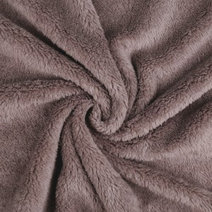 Könnte beinhalten: Nahaufnahme eines weichen, plüschigen Stoffes in einem gedämpften Mauve-Ton. Der Stoff ist gefaltet und verdreht, wodurch ein wirbelndes Muster entsteht.