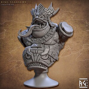 May include: Gray stone bust of a mythical creature with a large mouth, horns, and a long tongue. The bust is wearing a detailed headdress and armor. The bust is on a gray pedestal. The text "KING SGRAKKOR III COLLECTOR TIER" is at the top of the image.