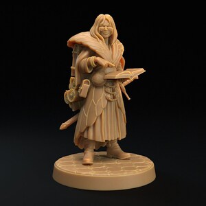 May include: A tan-coloured miniature figurine of a fantasy character, wearing glasses, a long coat, and holding a book. The figure has a backpack, a sword, and is standing on a circular base with a cobblestone pattern.