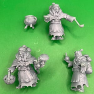 Könnte beinhalten: Vier unbemalte Miniaturfiguren einer Fantasy-Figur, jede mit einzigartigen Accessoires. Eine Figur hält eine Schöpfkelle und eine Schüssel, eine andere einen Korb mit Gegenständen und eine dritte eine Flasche. Ein kleiner Kessel ist ebenfalls vorhanden.
