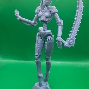 Könnte beinhalten: Eine graue, futuristische weibliche Figur mit mechanischen Details, die eine große gezahnte Klinge hält. Die Figur steht auf einem felsigen Sockel, mit beweglichen Gliedmaßen und einer rüstungsartigen Beschichtung. Der Hintergrund ist einfarbig grün.