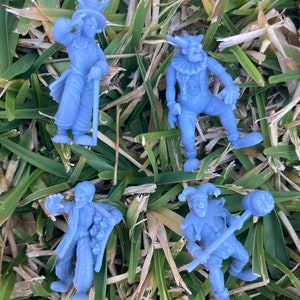 May include: Four blue plastic figurines of jesters, each with a different pose and expression. The figurines are standing on a bed of green grass.