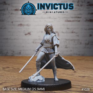 May include: A gray resin miniature figure of a warrior with long hair, wearing a wrap-style tunic, pants, and boots. The figure holds two straight rods in each hand and stands on a rock-like base. Text includes INVICTUS MINIATURES and BASE SIZE: MEDIUM (25.5MM).