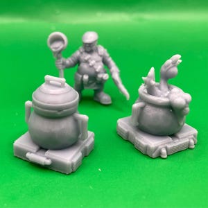 May include: A collection of gray miniature fantasy game figures, including a cauldron with a creature, a kettle, and a character holding a staff. The figures are on a green background.