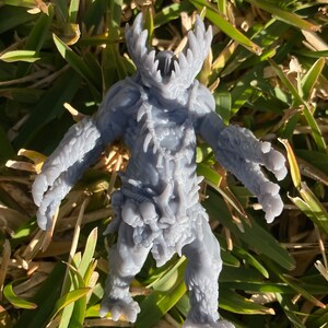 May include: A grey, detailed, 3D printed miniature of a creature with sharp teeth, claws, and a bony, spiky exterior. The creature is standing on a bed of green grass.