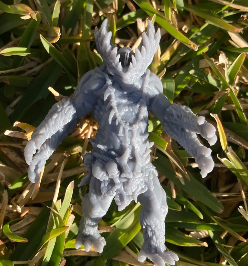 May include: A grey, detailed, 3D printed miniature of a creature with sharp teeth, claws, and a bony, spiky exterior. The creature is standing on a bed of green grass.