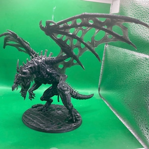 May include: A detailed black dragon figurine with large, intricate wings and a menacing pose. The dragon is standing on a round, textured base. The wings have a delicate, webbed design. The dragon's features include sharp claws, horns, and a detailed skeletal structure.