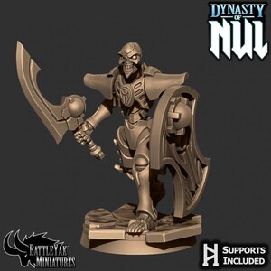 May include: A bronze-coloured miniature figure of a skeletal warrior from the "Dynasty of Nul" collection. The figure is armed with a large sword and shield, and is standing on a rocky base. The figure is labelled "BattleYak Miniatures" and "Supports Included".