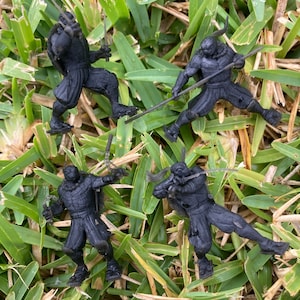 May include: Four black plastic action figures of Teenage Mutant Ninja Turtles, each with a different pose and weapon. The figures are posed on a bed of green grass.