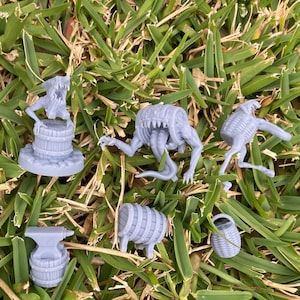 May include: A set of six grey 3D printed miniatures, including a monster, a barrel, a basket, an anvil, and two barrels. The miniatures are on a bed of green grass.