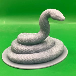Könnte beinhalten: Eine graue, 3D-gedruckte Schlangenfigur, die sich auf einer runden Basis zusammenrollt. Die Schlange hat eine strukturierte Oberfläche und ist mit erhobenem Kopf posiert.