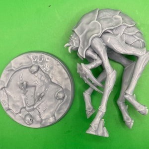 May include: A grey plastic miniature of a creature with a segmented body and multiple legs. The creature is posed in a crouched position with its legs bent. The miniature is on a grey plastic base with a textured surface.