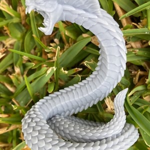 May include: A grey, 3D printed miniature of a serpent with a scaly body and an open mouth. The serpent is curled in a coil shape.