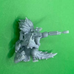 May include: A grey, detailed miniature figurine of a creature with a feathered tail, holding a rifle with a scope. The creature has a spiky, feathered head and is wearing armour.