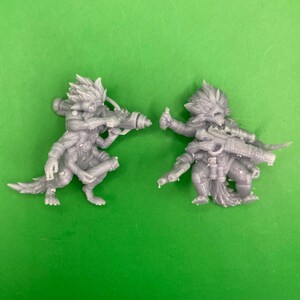 May include: Two grey, detailed, miniature figures of creatures with multiple arms and legs. One figure holds a gun, the other holds a rifle.