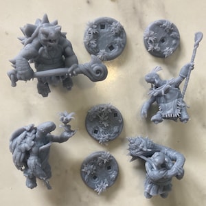 May include: A set of six grey 3D printed miniature figurines of turtles, including a turtle warrior holding a staff, a turtle warrior holding a sword, a turtle warrior holding a shield, a turtle warrior holding a spear, a turtle warrior holding a bow and arrow, and a turtle warrior holding a staff. The miniatures are on a white background.