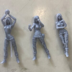 May include: Three grey 3D printed figurines of women in various poses. The figurines are detailed and have intricate designs.