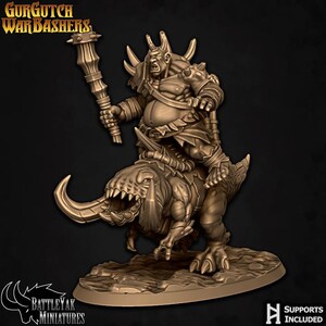 May include: A bronze miniature figure of a warrior riding a monstrous creature. The warrior holds a club and is adorned with armour and horns. The creature has large tusks and sharp teeth. The base of the figure has the text "BATTLE YAK MINIATURES" and "SUPPORTS INCLUDED".