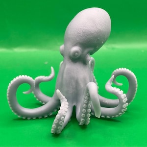 May include: A light grey octopus figurine with detailed tentacles and suckers. The octopus is posed upright against a bright green background. The figurine is a detailed representation of the marine animal.