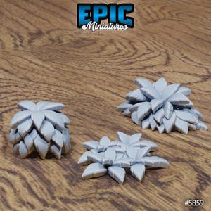 May include: Three light gray miniature plant models with a layered leaf design. The models are arranged on a wooden surface. The top left corner of the image has the text "EPIC Miniatures". The bottom right corner has the text "#5859".