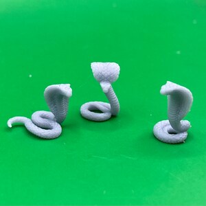 May include: Three grey plastic cobra figurines with raised hoods. The cobras are posed in different positions.
