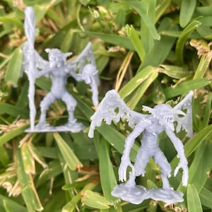 May include: Two grey 3D printed figurines of winged creatures with detailed textures. The figurines are posed with their wings spread out and have a menacing expression.