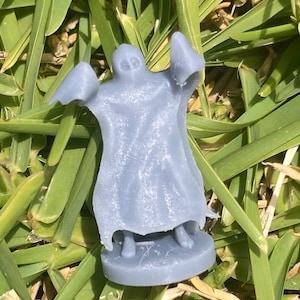 May include: A grey plastic ghost figurine with a flowing robe and outstretched arms. The figurine is standing on a round base.