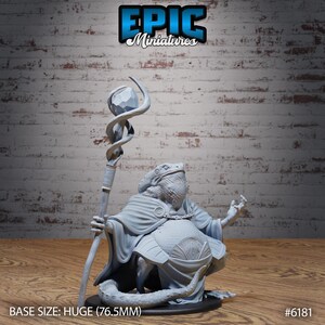 May include: A grey miniature figure of a lizard-like creature wearing a robe and holding a staff with a crystal. The base size is huge, measuring 7.65cm. The figure is from Epic Miniatures.