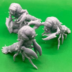May include: Three gray 3D printed figurines of a creature with a lobster-like body and a human-like head. The figurines are posed in different positions, with one standing upright, one crouching, and one lying down.
