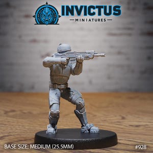 May include: A gray miniature figure of a soldier in a combat stance, holding a rifle. The figure is on a black base. The text "INVICTUS - MINIATURES -" and a logo are at the top. The base size is medium (25.5mm).