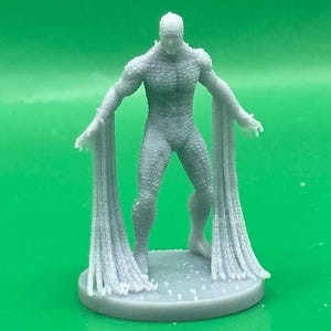 May include: A grey figurine of a humanoid creature with a textured, scaly appearance. The figure stands on a circular base and has long, flowing appendages extending from its arms. The design suggests a fantasy or science fiction theme.