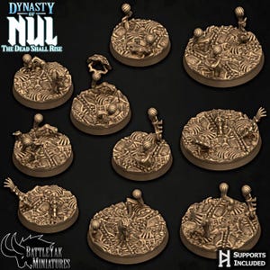 May include: A set of bronze-coloured miniature bases with detailed, textured designs. Each base has a circular shape with intricate relief patterns, including skeletal or mechanical elements. The bases are designed for miniature figures, with the text "SUPPORTS INCLUDED".
