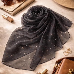May include: A black scarf with a constellation pattern, arranged in a spiral. The scarf is surrounded by accessories, including sunglasses, a hat, a purse, and perfume.