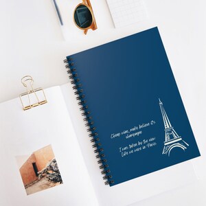 May include: A dark blue spiral notebook with a white outline of the Eiffel Tower and the text "Cheap wine, make believe it's champagne. I was taken by the view like we were in Paris."