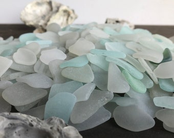 May include: A pile of sea glass in various shades of blue and white. The glass pieces are smooth and have been tumbled by the ocean.