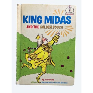 May include: Vintage children's book titled "King Midas and the Golden Touch." The cover features an illustration of King Midas in a yellow outfit, pointing upwards. The background includes green grass and red flowers. The book is part of the "Beginner Books" series.