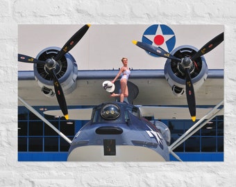 May include: A woman in a white swimsuit stands on the nose of a blue and white seaplane. The seaplane has two large propellers and a red star on the fuselage. The seaplane is parked in a hangar.