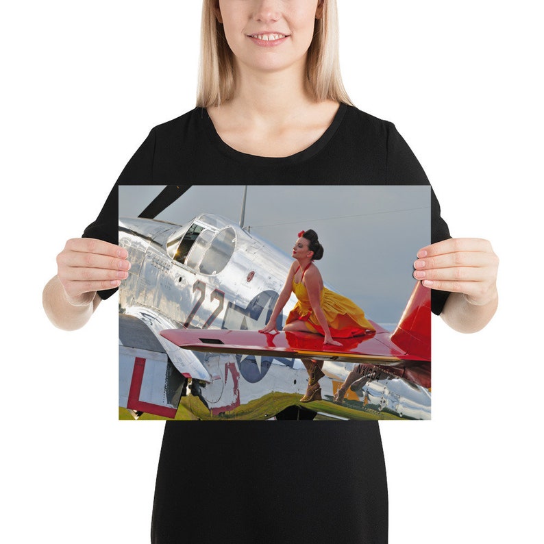 May include: A woman in a yellow and red dress sits on the wing of a silver and red airplane. The airplane has the number "22" on the side.
