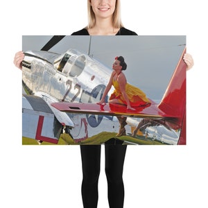 May include: A woman in a yellow and red dress sits on the wing of a silver and red airplane. The airplane has the number 22 on the side and a star on the wing.